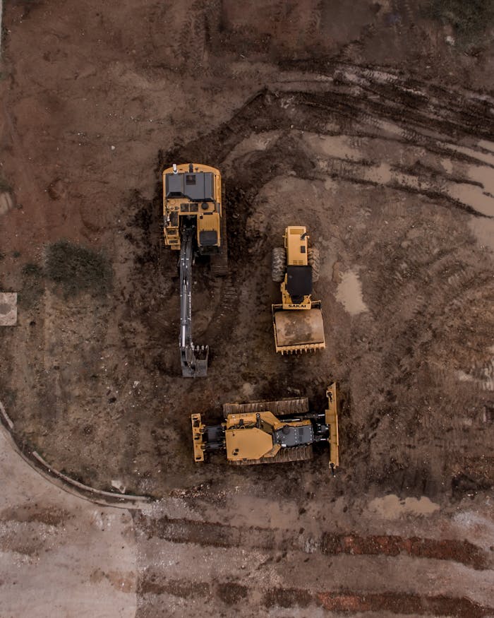 about-us-02 An aerial shot of heavy machinery at a construction site, including excavators and road rollers.