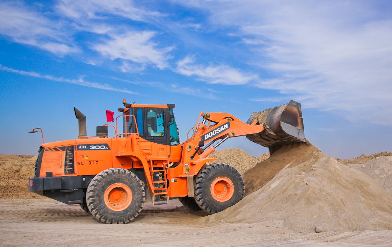 about-us-01 An orange bulldozer at work, moving sand under a clear blue sky on a construction site.